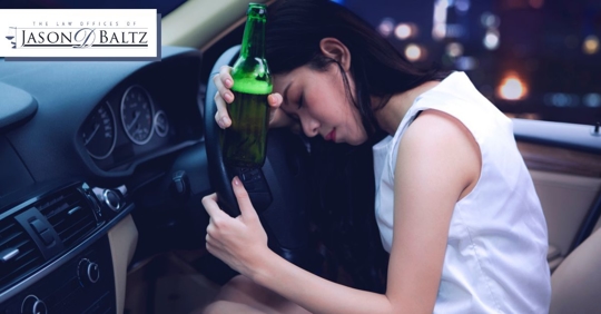 Woman holding a wine bottle and slumped over the driving wheel